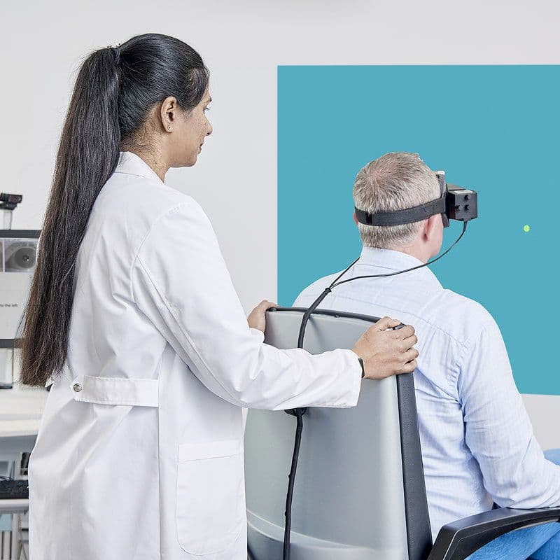 Specialista che esegue un test cervico-oculare su un paziente seduto nella poltrona rotante reclinabile Orion e con indosso la maschera VisualEyes VNG